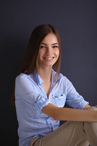 Jonge vrouw zittend op de vloer geïsoleerd donkere achtergrond — Stockfoto