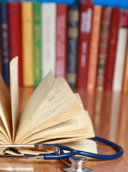 Stethoscope está acostado con un libro en el escritorio contra los libros —  Fotos de Stock