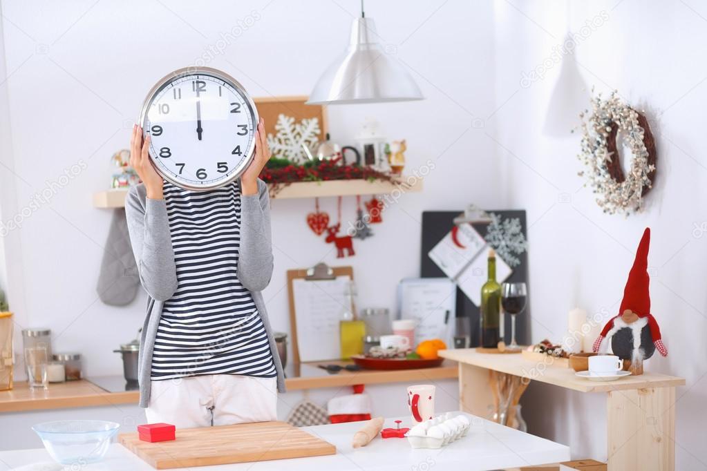 Happy young woman showing clock in christmas decorated kitchen