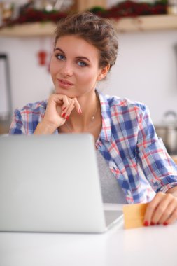 Mutfakta bilgisayar ve kredi kartı kullanan gülümseyen bir kadın.