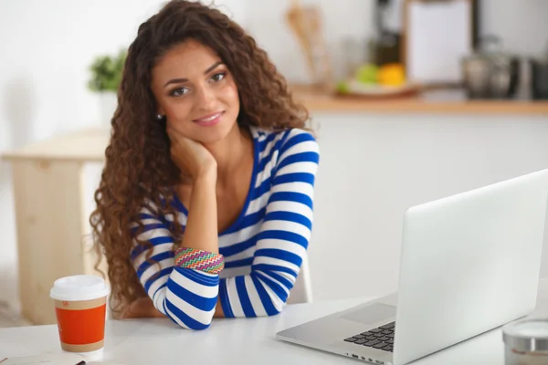 Mujer joven sonriente con taza de café y portátil en la cocina en casa — Foto de Stock