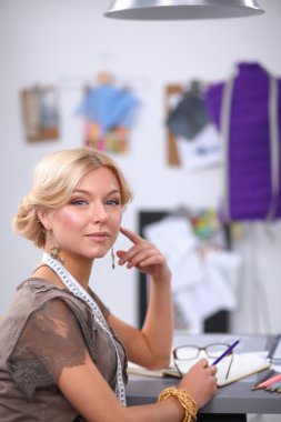 Gülümseyen kadın moda tasarımcısı ofis masasında oturuyor.