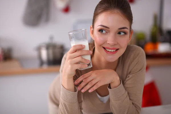 Smiling young woman drinking milk, standing in the kitchen — Stock Photo, Image