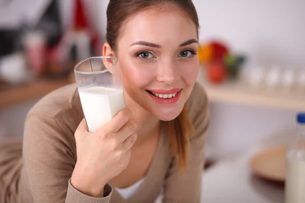 Sorridente giovane donna che beve latte, in piedi in cucina — Foto Stock