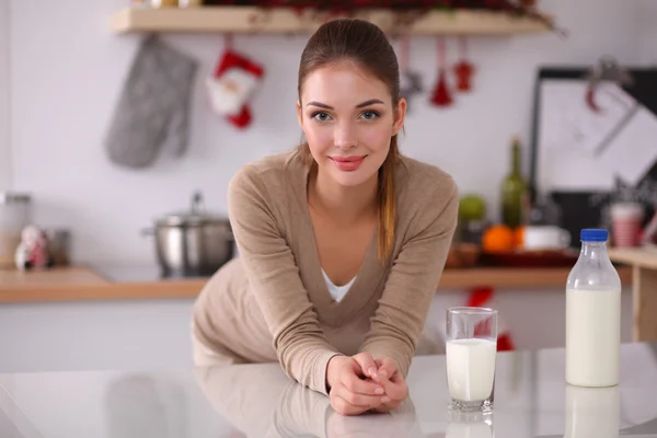 Sorridente giovane donna che beve latte, in piedi in cucina — Foto Stock