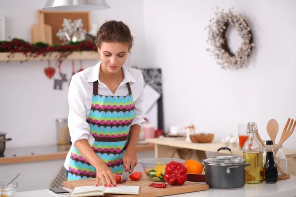 Mutfakta yemek kitabı okuyan genç bir kadın yemek tarifi arıyor. — Stok fotoğraf