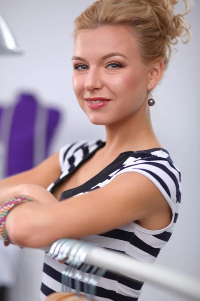 Beautiful young stylist near rack with hangers — Stock Photo, Image