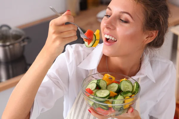 Mujer joven comiendo ensalada fresca en la cocina moderna — Foto de Stock