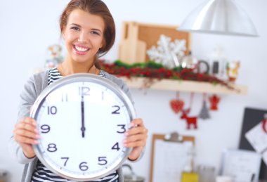 Mutlu genç kadın Noel süslemeli mutfakta saat gösteriyor.