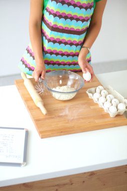 Mutfakta gülümseyen genç bir kadın, arka planda soyutlanmış.