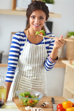 Genç kadın modern mutfakta taze salata yiyor.