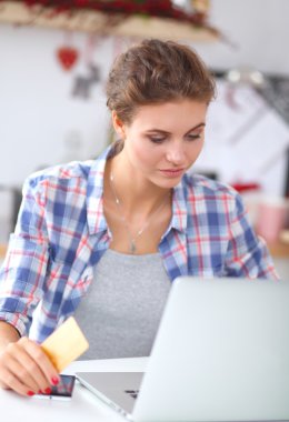 Mutfakta bilgisayar ve kredi kartı kullanan gülümseyen bir kadın.