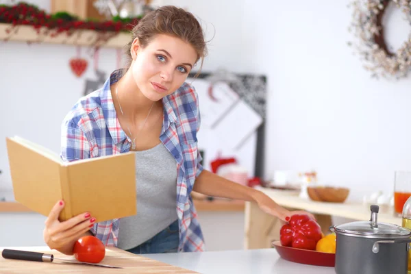 Jovem mulher lendo livro de receitas na cozinha, à procura de receita — Fotografia de Stock