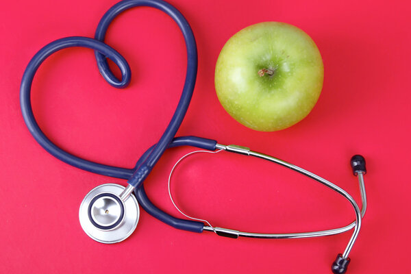 Green apple and stethoscope isolated on red background.
