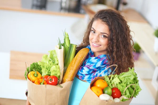 Mujer joven sosteniendo bolsa de la compra de comestibles con verduras de pie en la cocina. — Foto de Stock