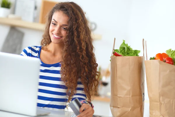 Lachende vrouw online winkelen met behulp van computer en creditcard in de keuken — Stockfoto