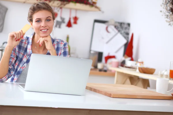 Mulher sorrindo compras on-line usando computador e cartão de crédito na cozinha — Fotografia de Stock