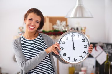 Mutlu genç kadın Noel süslemeli mutfakta saat gösteriyor.