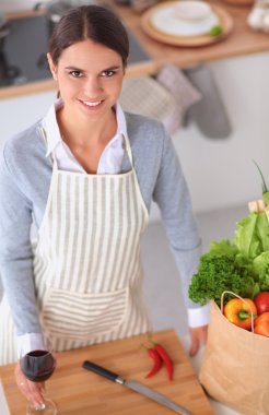 Mutfakta alışveriş torbaları olan bir kadın, masanın yanında duruyor.