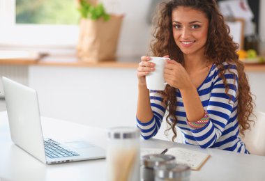 kahve fincanı ve dizüstü evde mutfakta gülümseyen genç kadın