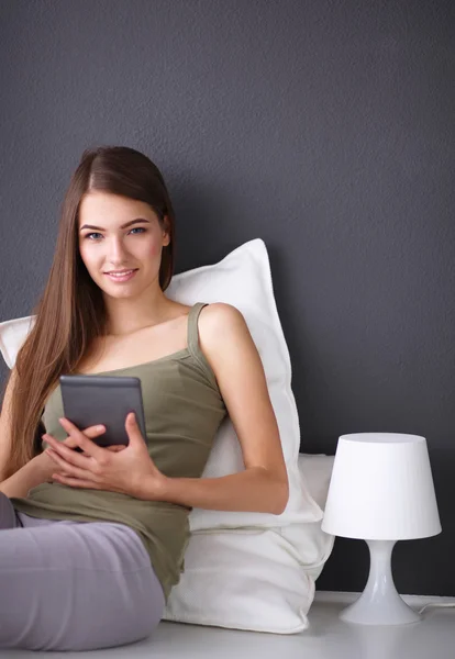 Mujer morena bonita sentada en el suelo con una almohada y mesa de avión — Foto de Stock