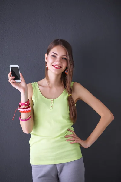 Smuk ung kvinde holdiing mobiltelefon, isoleret på grå - Stock-foto
