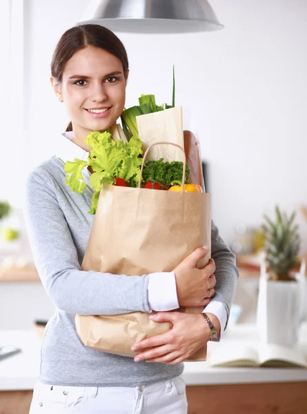 Sebzeli alışveriş poşeti taşıyan genç bir kadın mutfakta duruyor.. — Stok fotoğraf