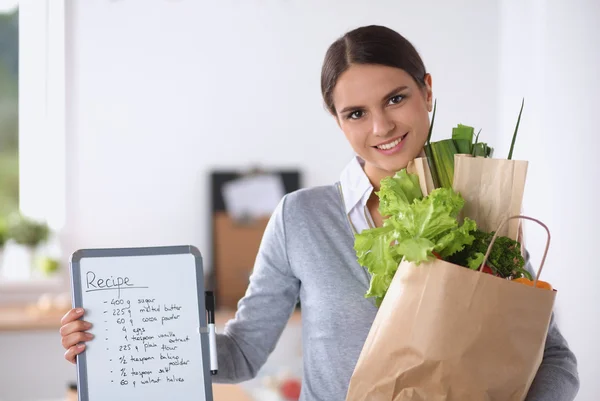 Молода жінка тримає продуктовий сумку з овочами стоїть на кухні . — стокове фото