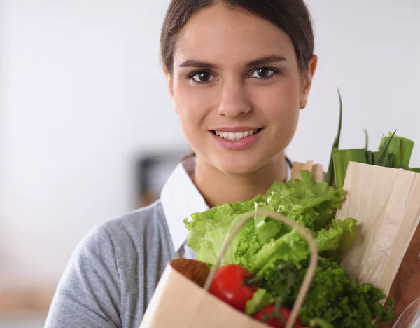 Молода жінка тримає продуктовий сумку з овочами стоїть на кухні . — стокове фото