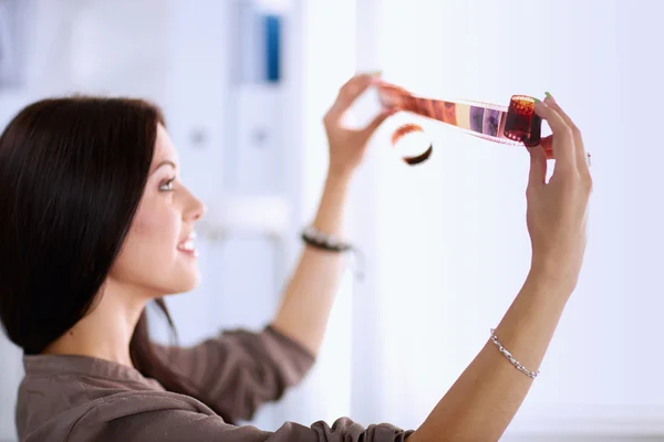 Young woman watching footage on film, standing near window — Stock Photo, Image