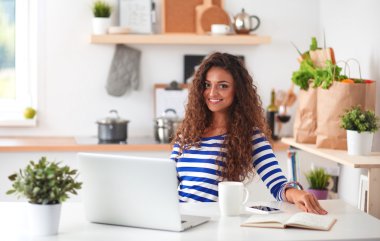 kahve fincanı ve dizüstü evde mutfakta gülümseyen genç kadın