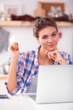 Smiling woman online shopping using computer and credit card in kitchen clipart