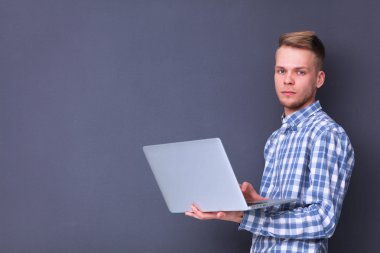 Gri arka plan üzerinde dizüstü bilgisayar konumu olan kendine güvenen genç adam portresi