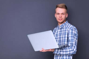 Gri arka plan üzerinde dizüstü bilgisayar konumu olan kendine güvenen genç adam portresi