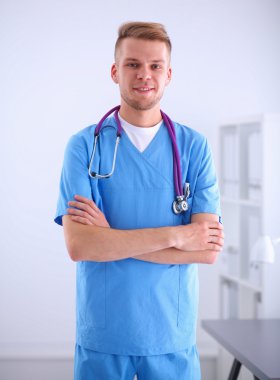 Steteskoplu doktor ayakta, çapraz kollu, beyaz arka planda izole.