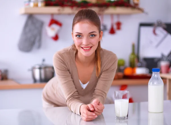 Sorridente giovane donna che beve latte, in piedi in cucina — Foto Stock