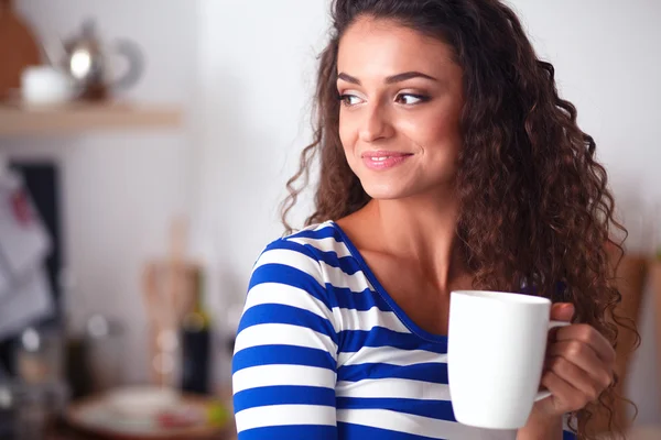 Portrait of young woman with cup against kitchen interior background. — Stock Photo, Image