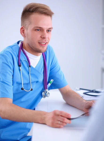 Портрет улыбающегося врача-мужчины с ноутбуком, сидящего за столом в медицинском кабинете — стоковое фото
