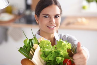 Elinde sebzeli alışveriş poşeti olan genç bir kadın.