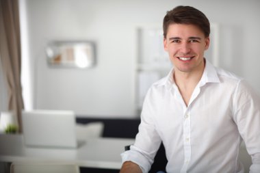 Genç işadamı ofiste çalışıyor, masada oturuyor.