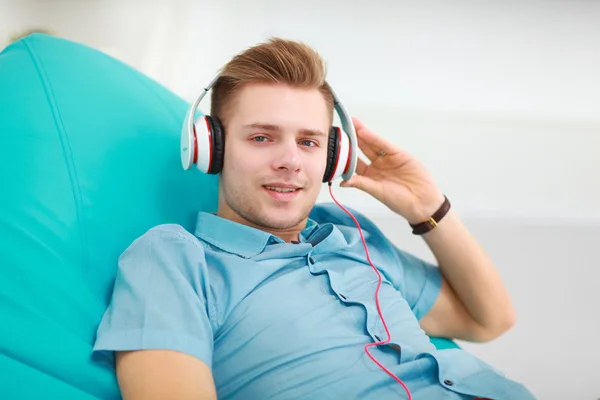 Homem ouvindo música em fone de ouvido no sofá em casa — Fotografia de Stock