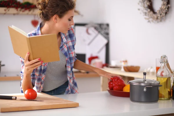 Jonge vrouw die kookboek leest in de keuken, op zoek naar recept — Stockfoto