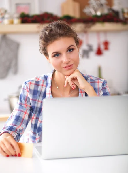 Mujer sonriente compras en línea utilizando la computadora y la tarjeta de crédito en la cocina — Foto de Stock