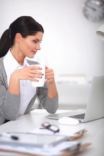 Молодая деловая женщина сидит на столе с чашкой в офисе — стоковое фото