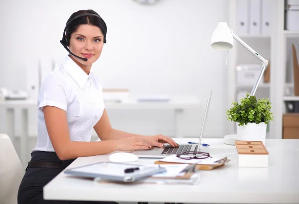 Retrato de mulher de negócios bonita trabalhando em sua mesa com fone de ouvido e laptop — Fotografia de Stock