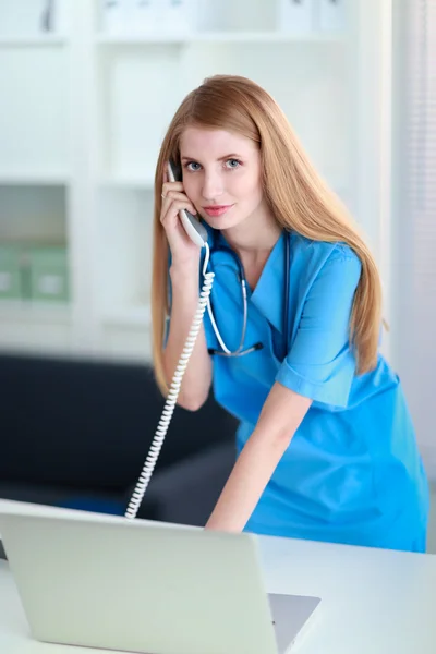 Junge Ärztin im weißen Kittel telefoniert am Computer — Stockfoto