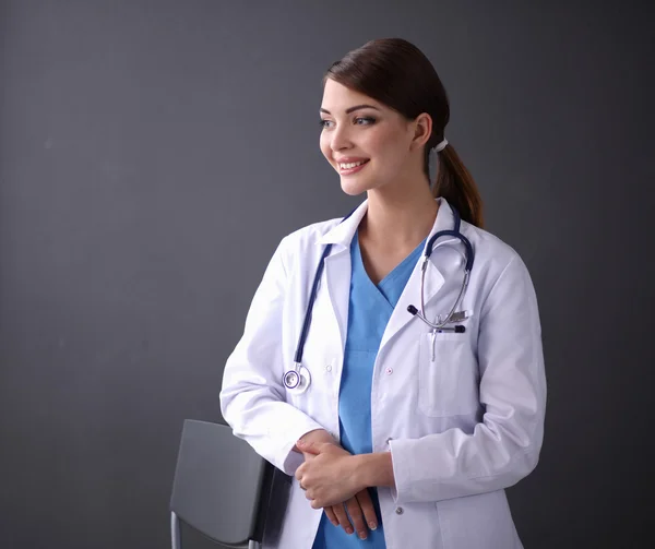 Médico fêmea bonita em pé perto de fezes isolado fundo cinza — Fotografia de Stock