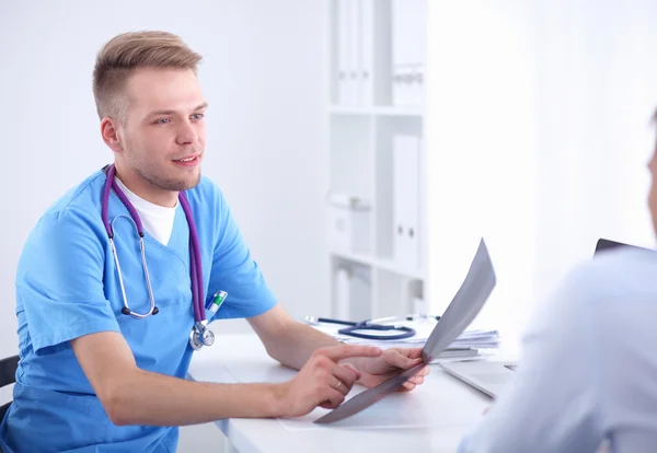 Retrato de um médico masculino sorridente com laptop sentado na mesa no consultório médico — Fotografia de Stock