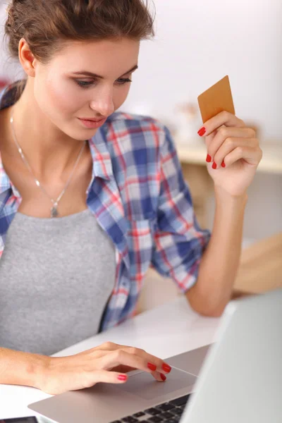 Улыбающаяся женщина совершала интернет-покупки с помощью компьютера и кредитной карты на кухне — стоковое фото