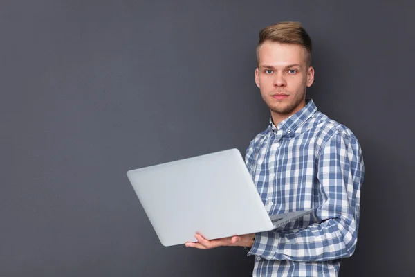 ग्रे पृष्ठभूमि पर खड़े लैपटॉप के साथ आत्मविश्वास वाले युवा का चित्र — स्टॉक फ़ोटो, इमेज